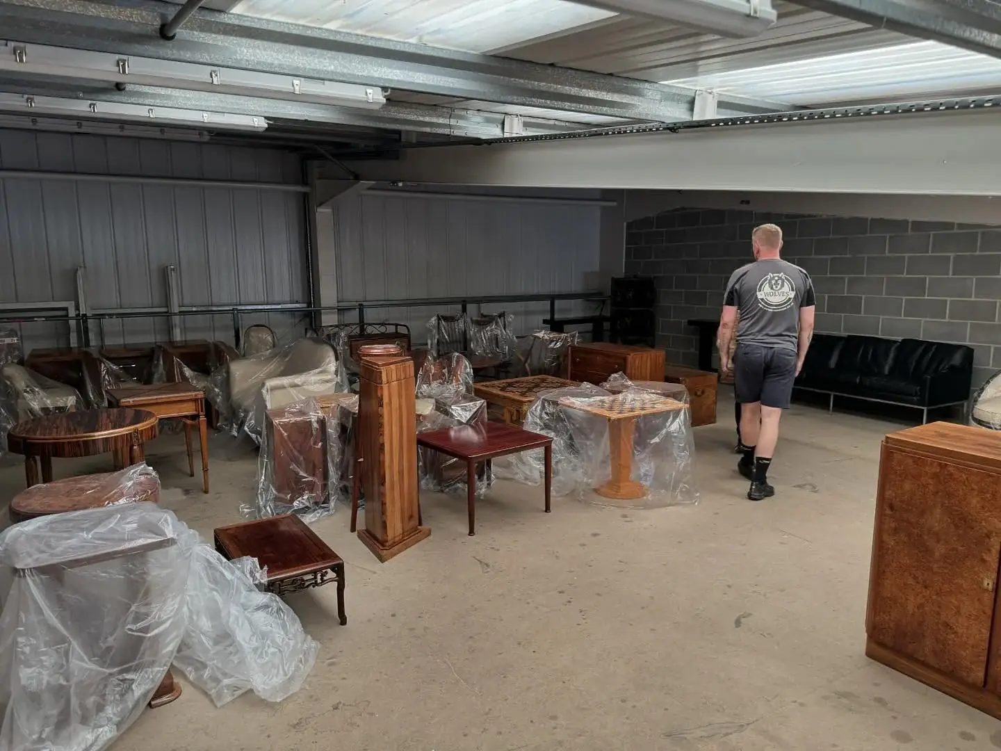 A Wolves Removals crew member among wrapped antique tables, chairs and cabinets in a warehouse during unloading