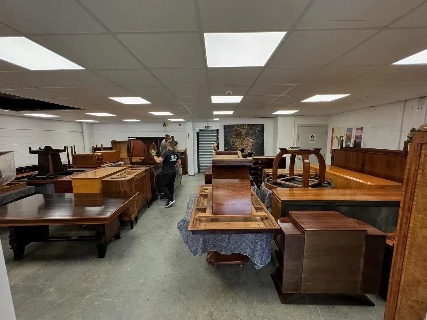 Polished Art Deco furniture including veneered tables, sideboards and cabinets set out in a bright new showroom after being moved