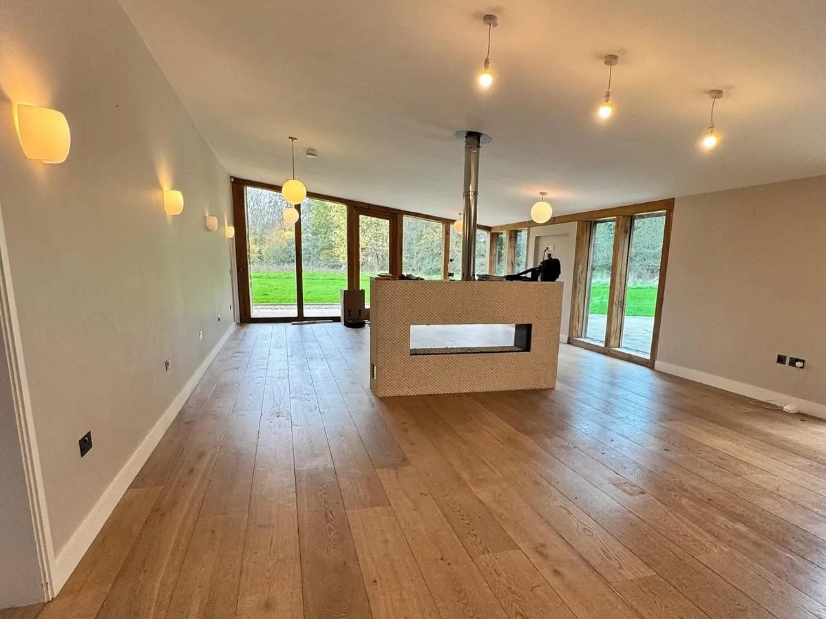 A large open-plan living space in a barn conversion with an oak floor, wood-burner flue and full-height glazing onto the garden