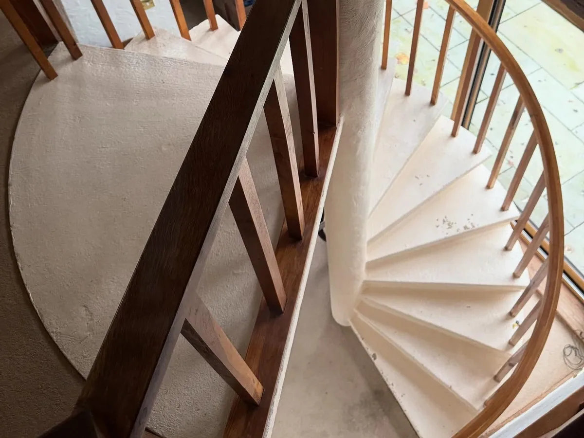 Looking down a tight spiral staircase with a curved wooden balustrade in a barn conversion