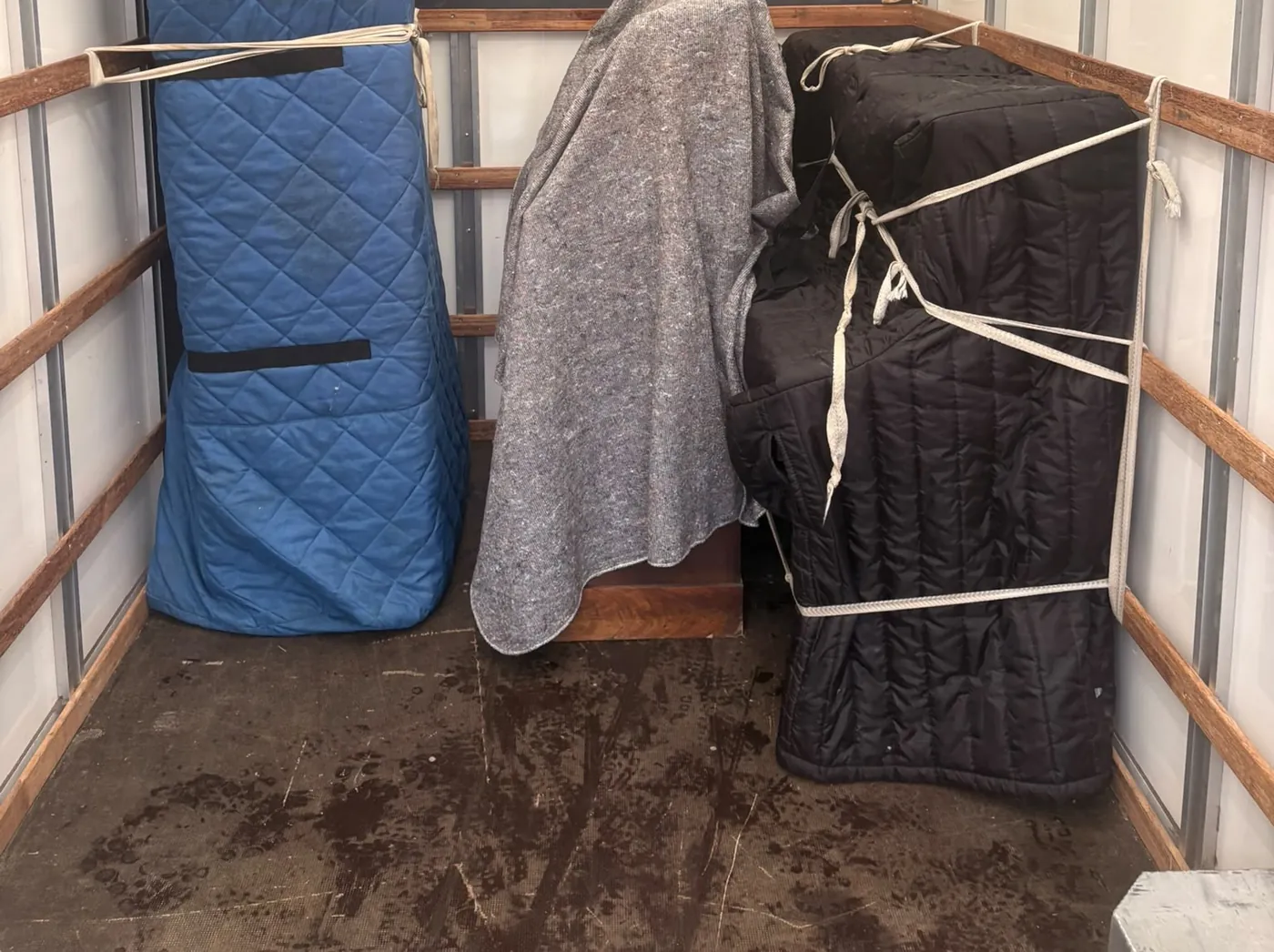 Inside a Luton van: tall pieces in blue and black quilted covers and a grey blanket, strapped to the side rails