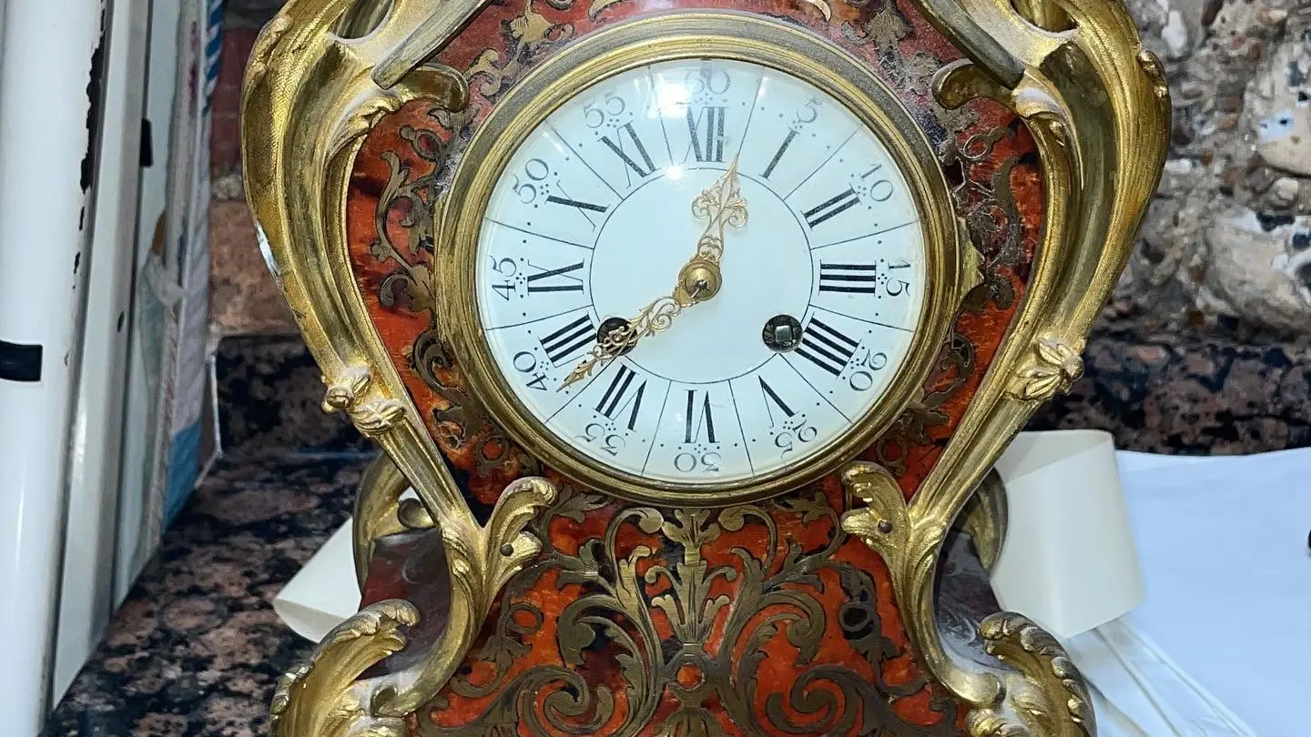 A red boulle bracket clock with gilt ormolu mounts and an enamel dial on a stone worktop