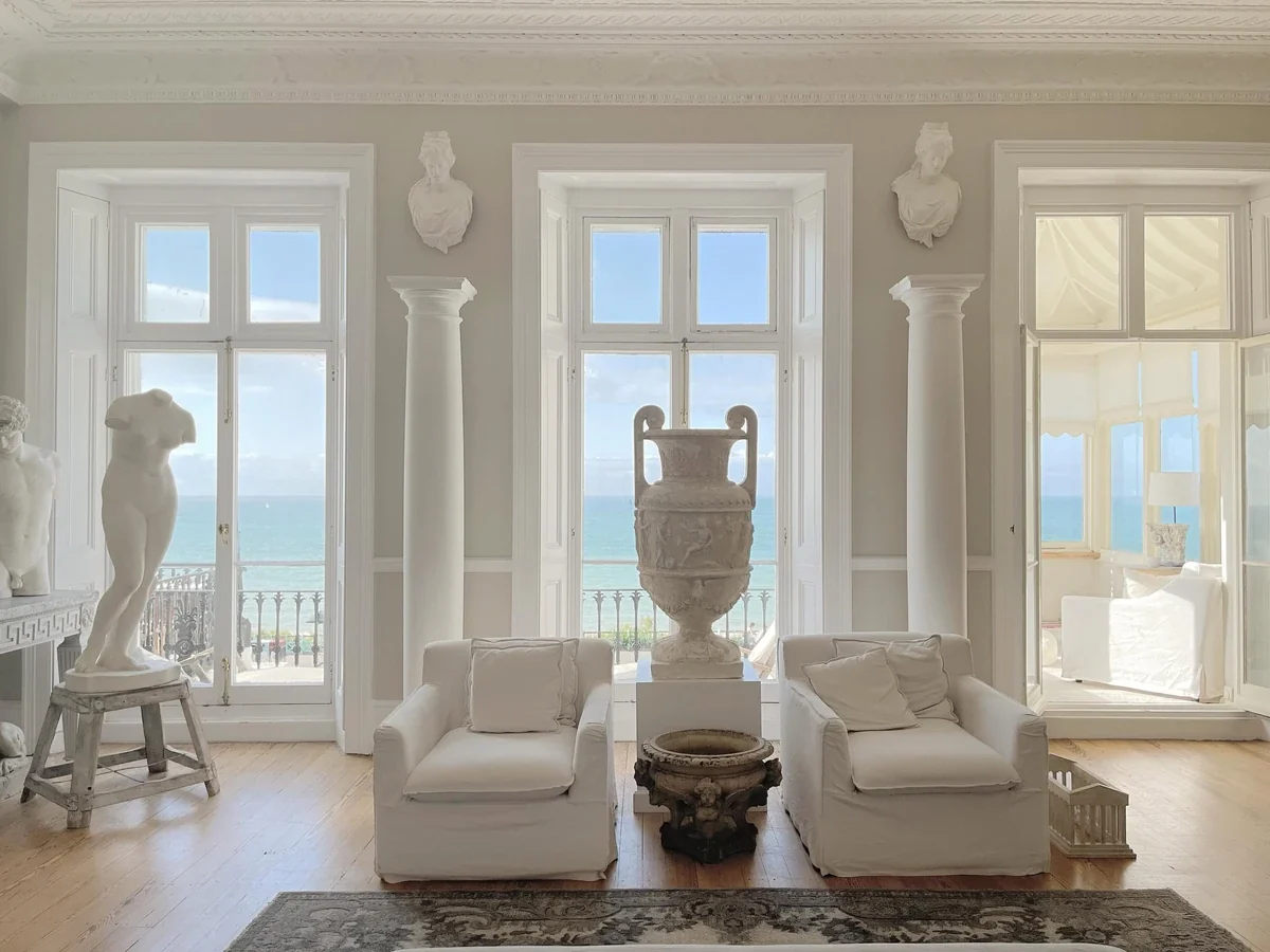 A Brighton seafront drawing room with classical sculpture and a sea view through open French windows
