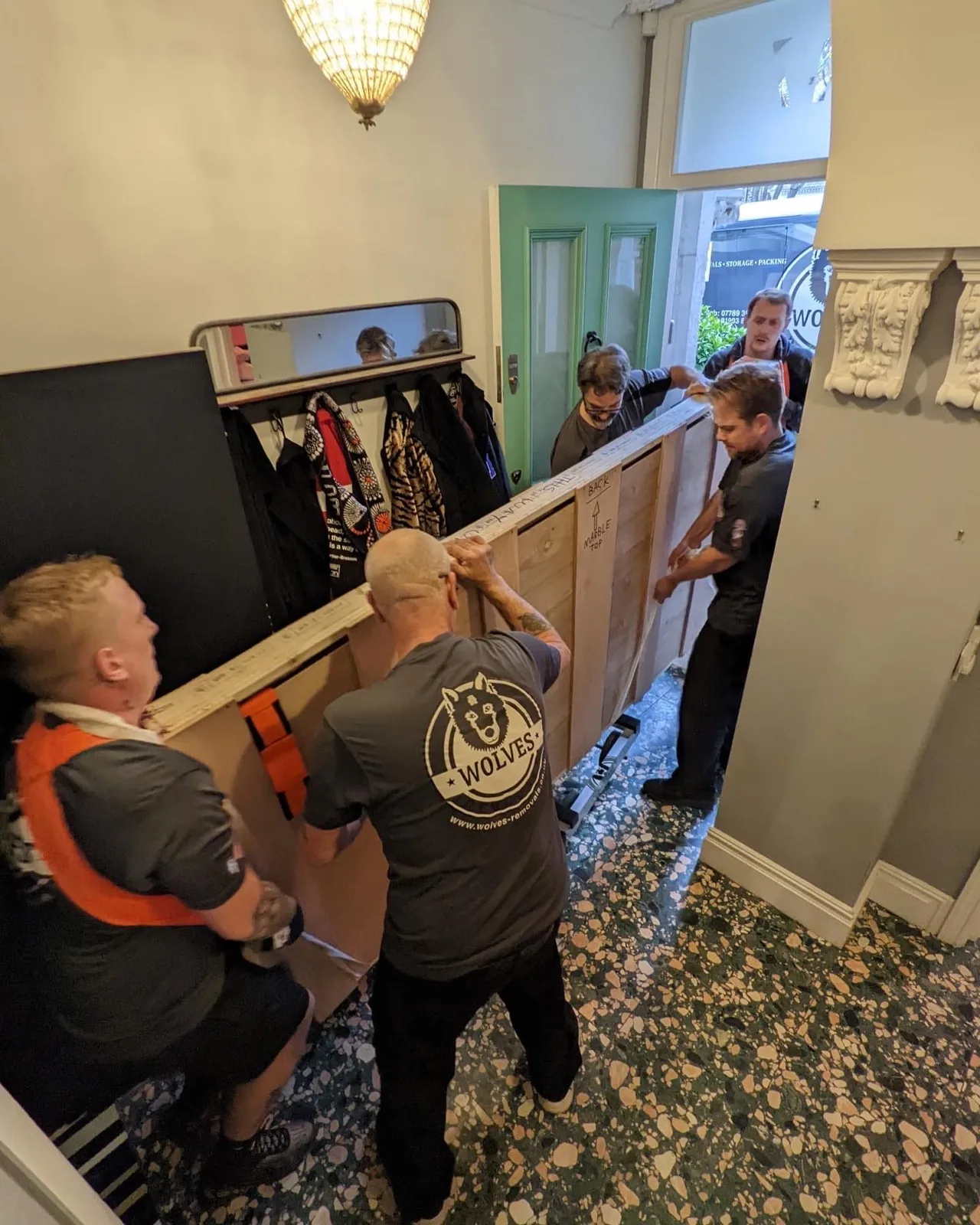 Two movers carrying a wardrobe through a house hallway