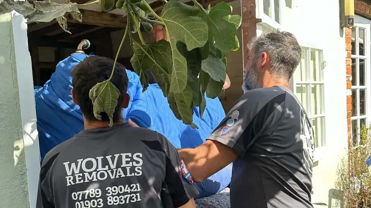 Two Wolves Removals crew passing a wrapped sofa through a window opening in Chichester