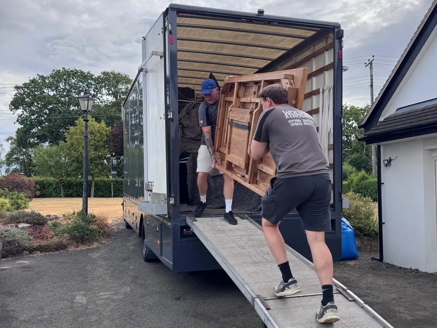 Two Wolves Removals crew members carrying a wooden table up the lorry ramp