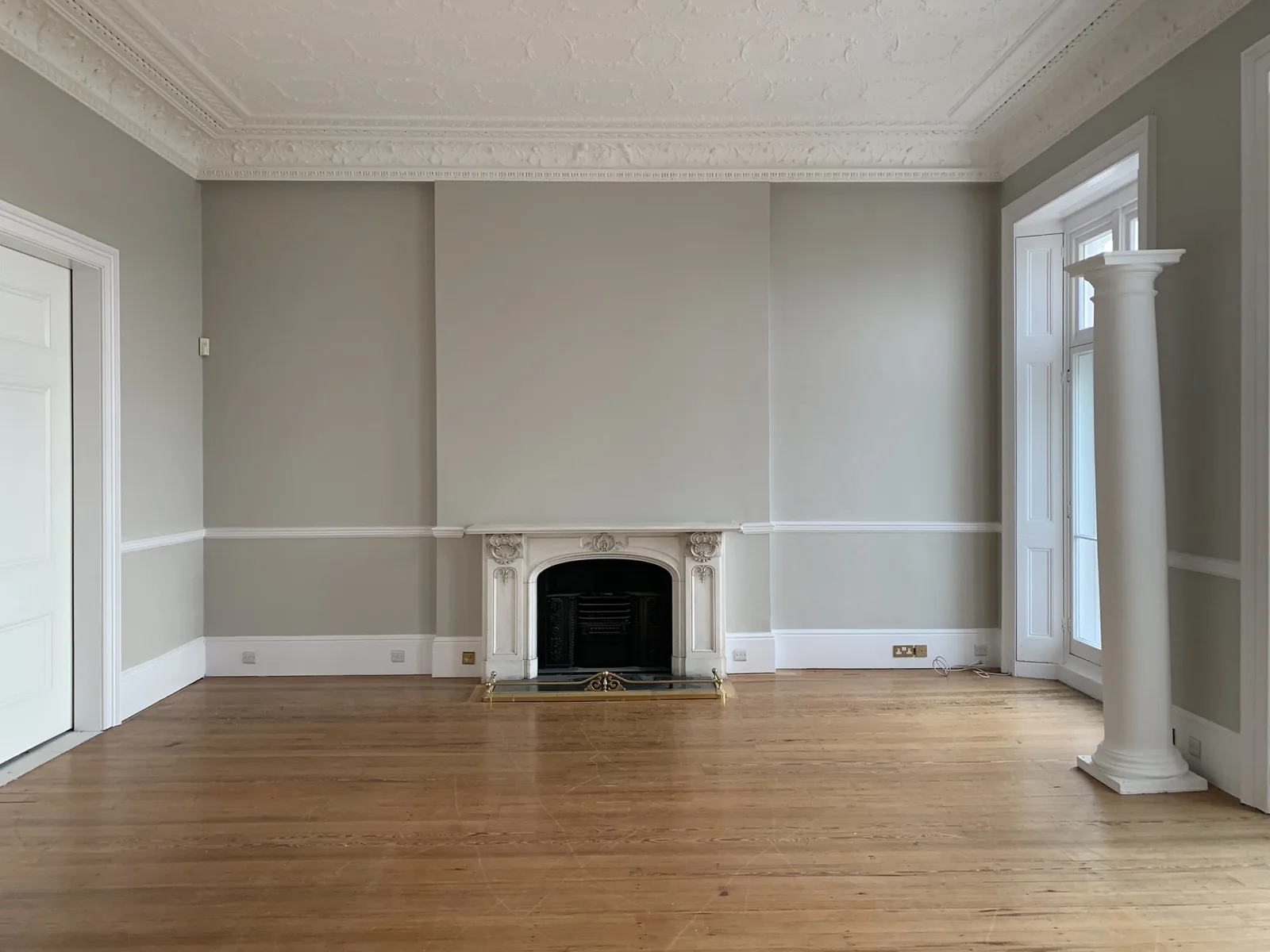 An emptied period sitting room with bare floorboards and a carved fireplace