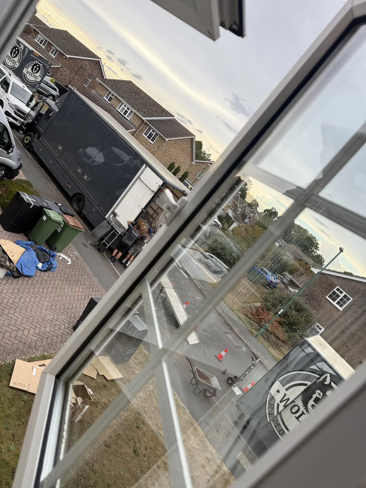 View from an upstairs window at dusk of a Wolves Removals lorry and van with flattened cartons on the drive