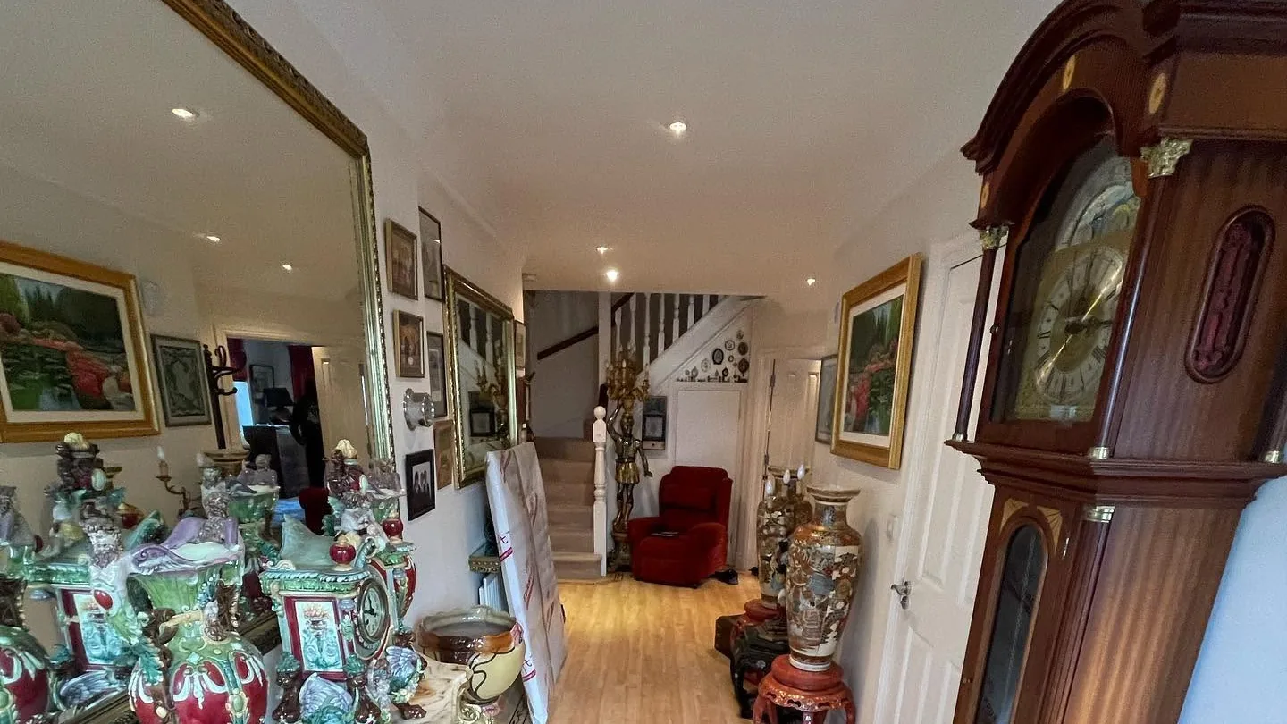 A mahogany longcase clock in a hallway of antiques, beside a wrapped item ready for a house move