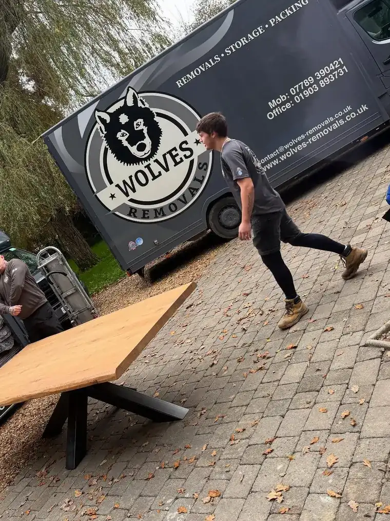 A Wolves Removals crew member loading a large oak dining table onto a lorry tail lift during a Horsham house move