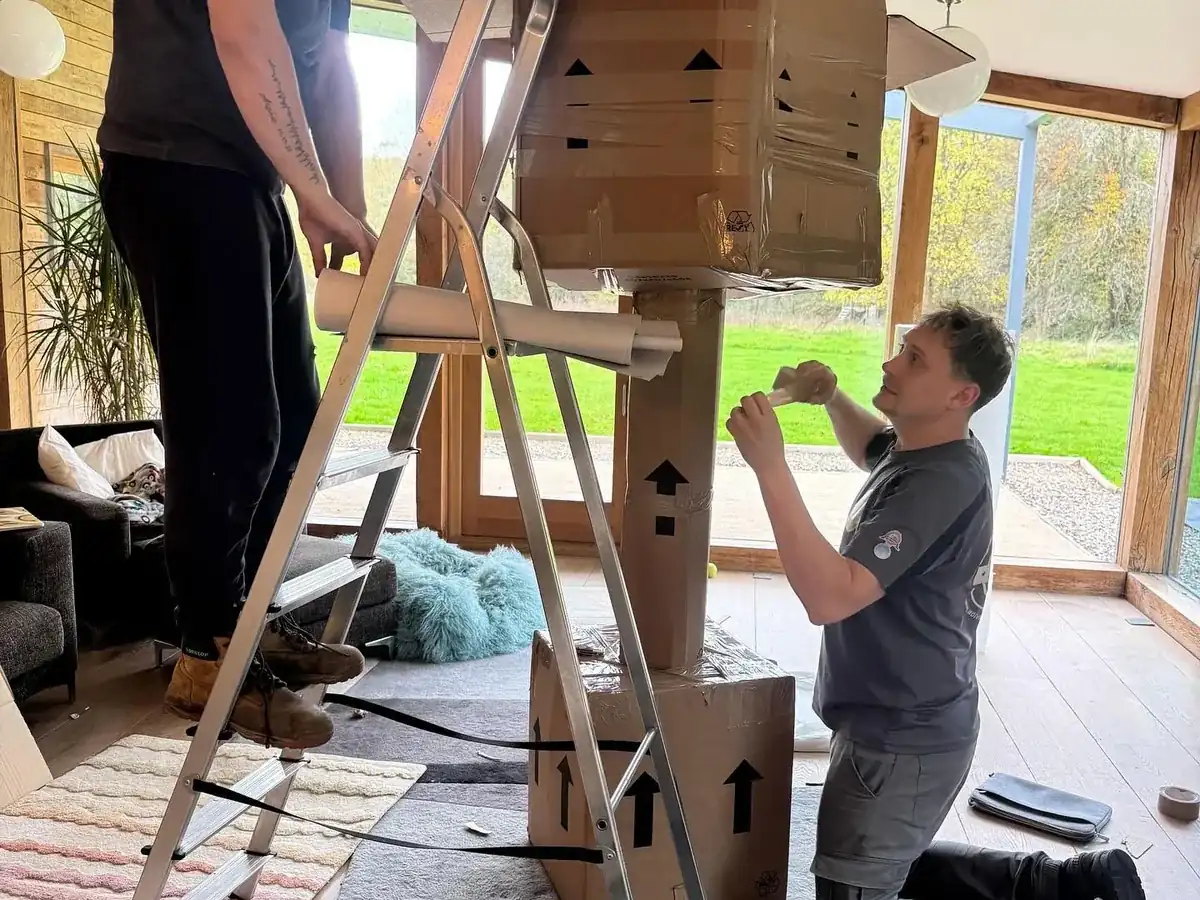 Two Wolves Removals packers boxing and wrapping a tall floor lamp during a full packing service at a house in Horsham