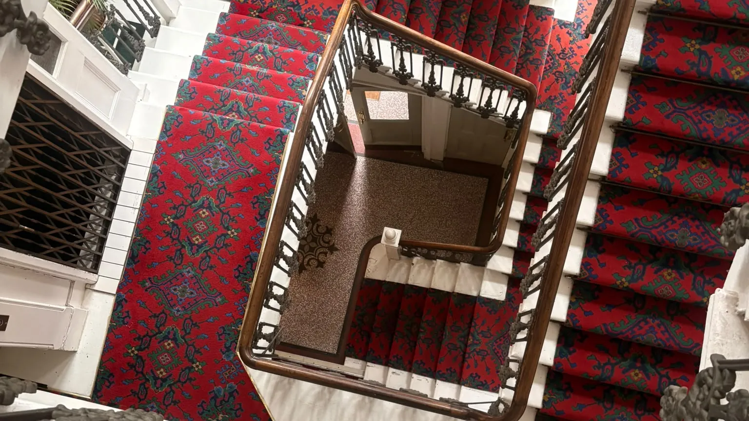 Looking down a red-carpeted period staircase with iron balusters and a wooden handrail in a Hove mansion block