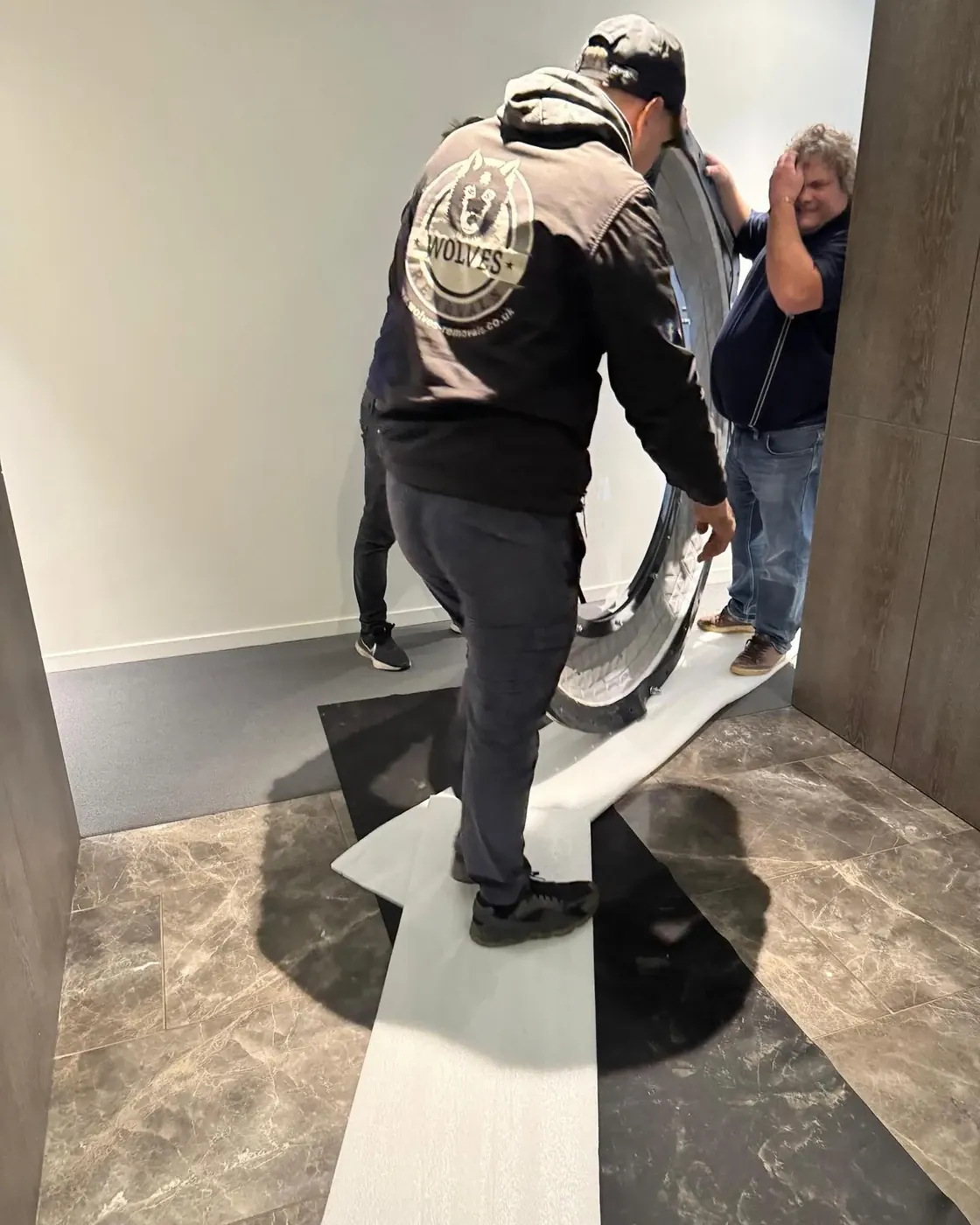 Two removal crew carrying a curved end section of a hyperbaric chamber along a corridor
