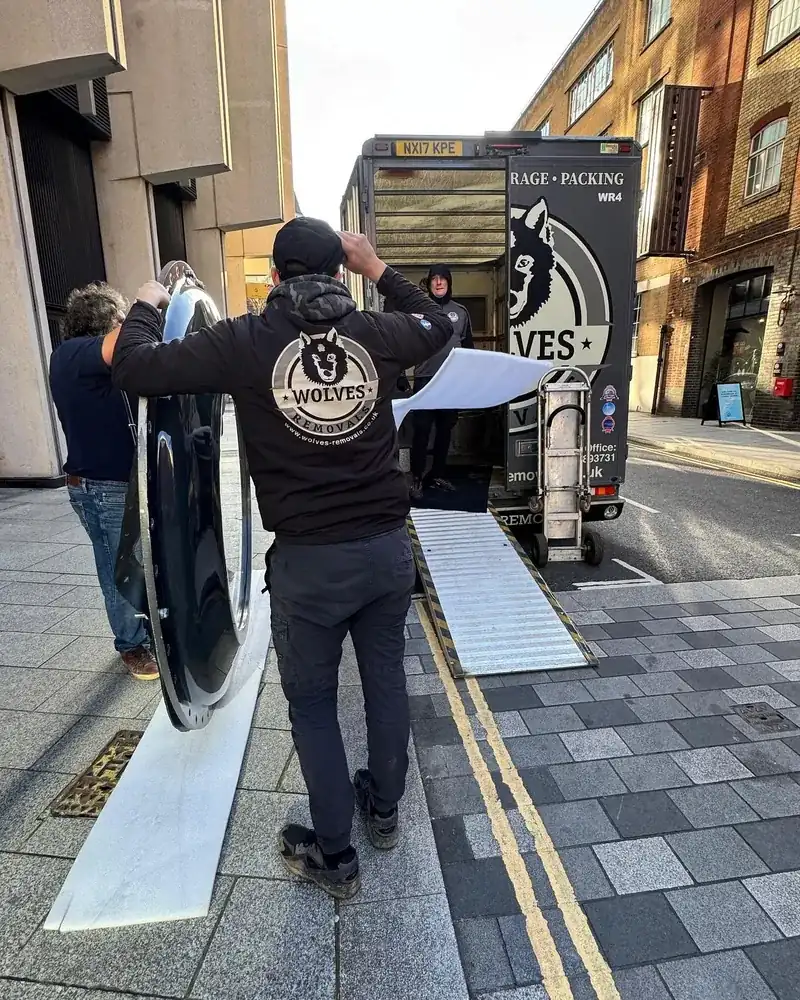 A Wolves Removals crew carrying a curved chamber section up a ramp into a lorry on a narrow London street