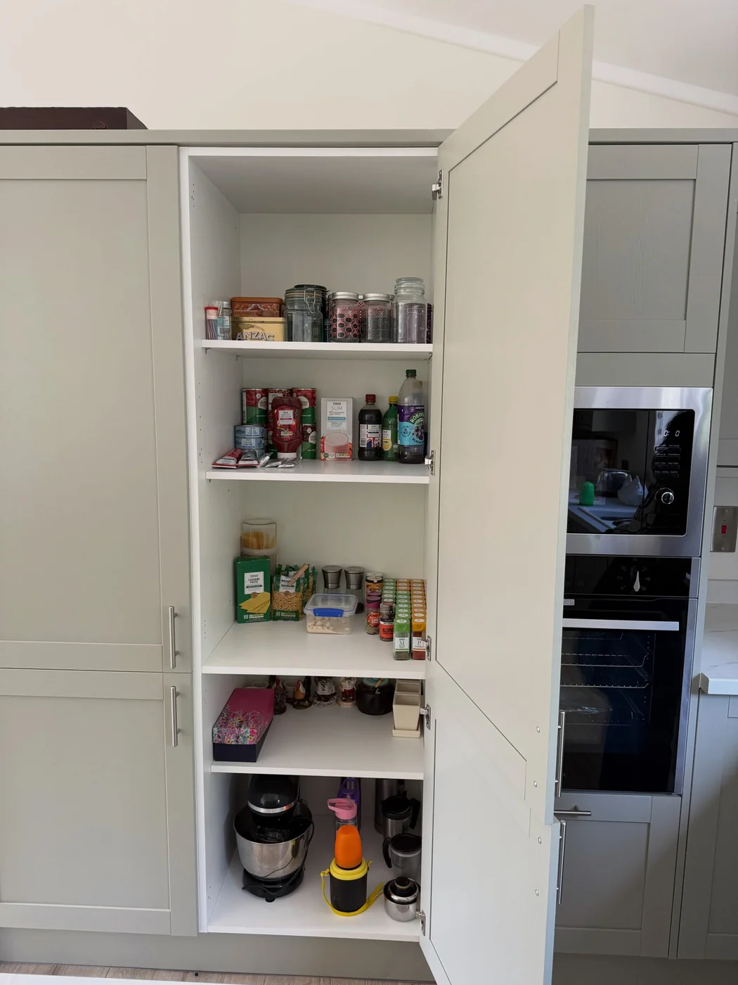 Fitted larder cupboard restocked with food, jars and appliances after a house move
