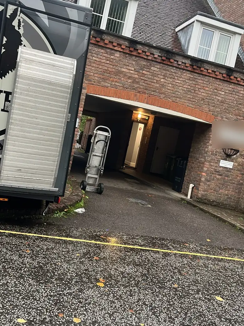 Low brick archway leading to a block of flats, with a sack truck in front and a van beside it