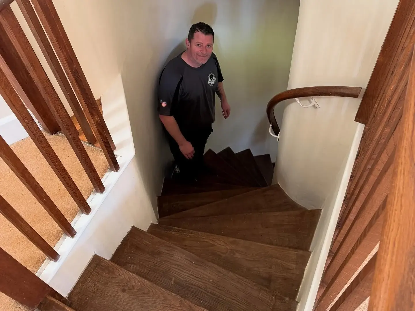 Looking down a curved staircase with tapered winder treads and a Wolves Removals crew member standing at the turn
