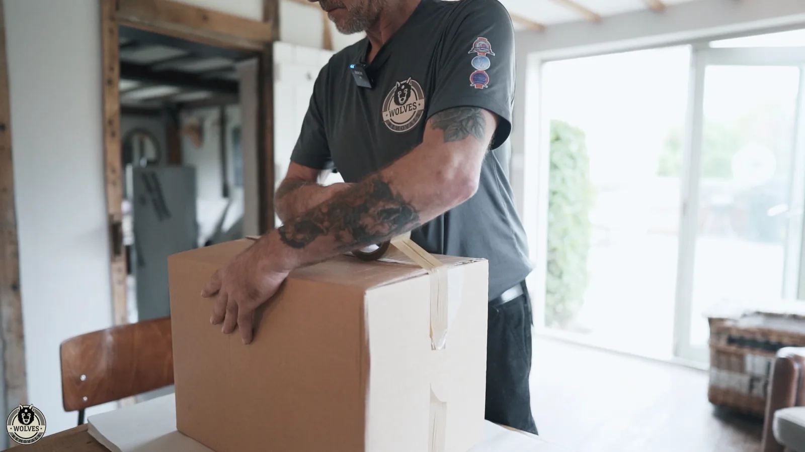 Wolves Removals mover in a branded polo closing the top flaps of a large cardboard box