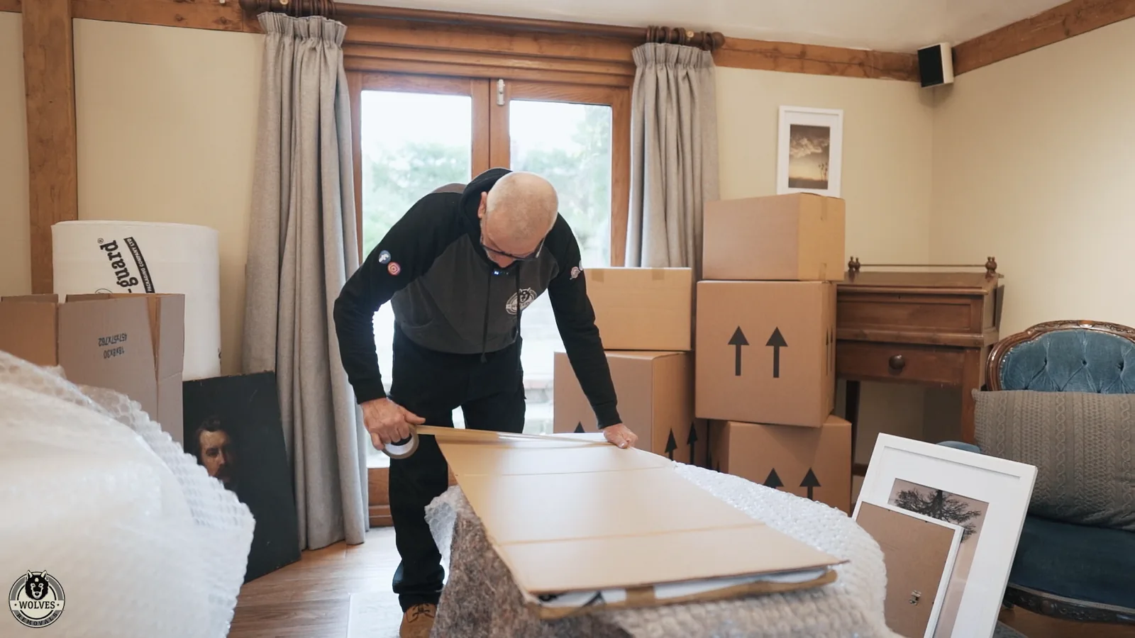 Mover wrapping a table top in protective covering in a room stacked with cardboard boxes