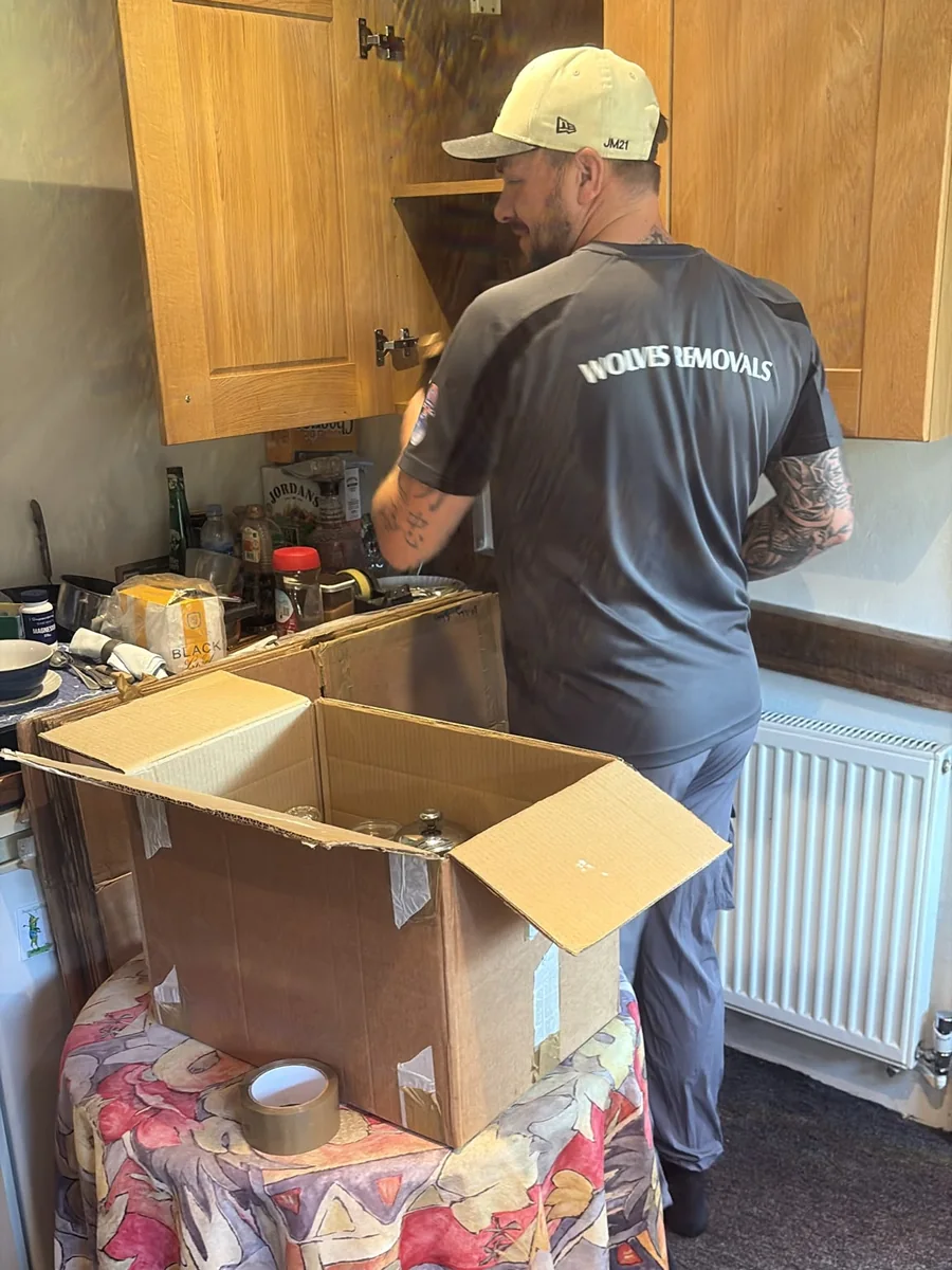 Wolves Removals packer in a branded T-shirt emptying a kitchen cupboard into an open moving box
