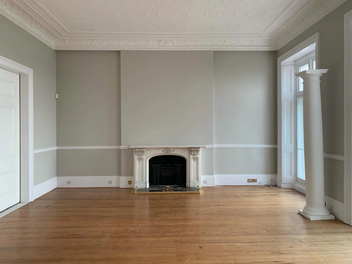 An empty period drawing room with a marble fireplace and original floorboards