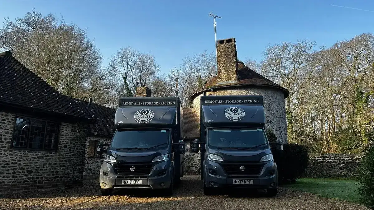 Two Wolves Removals vans outside a round flint house with a conical roof during a Pulborough move