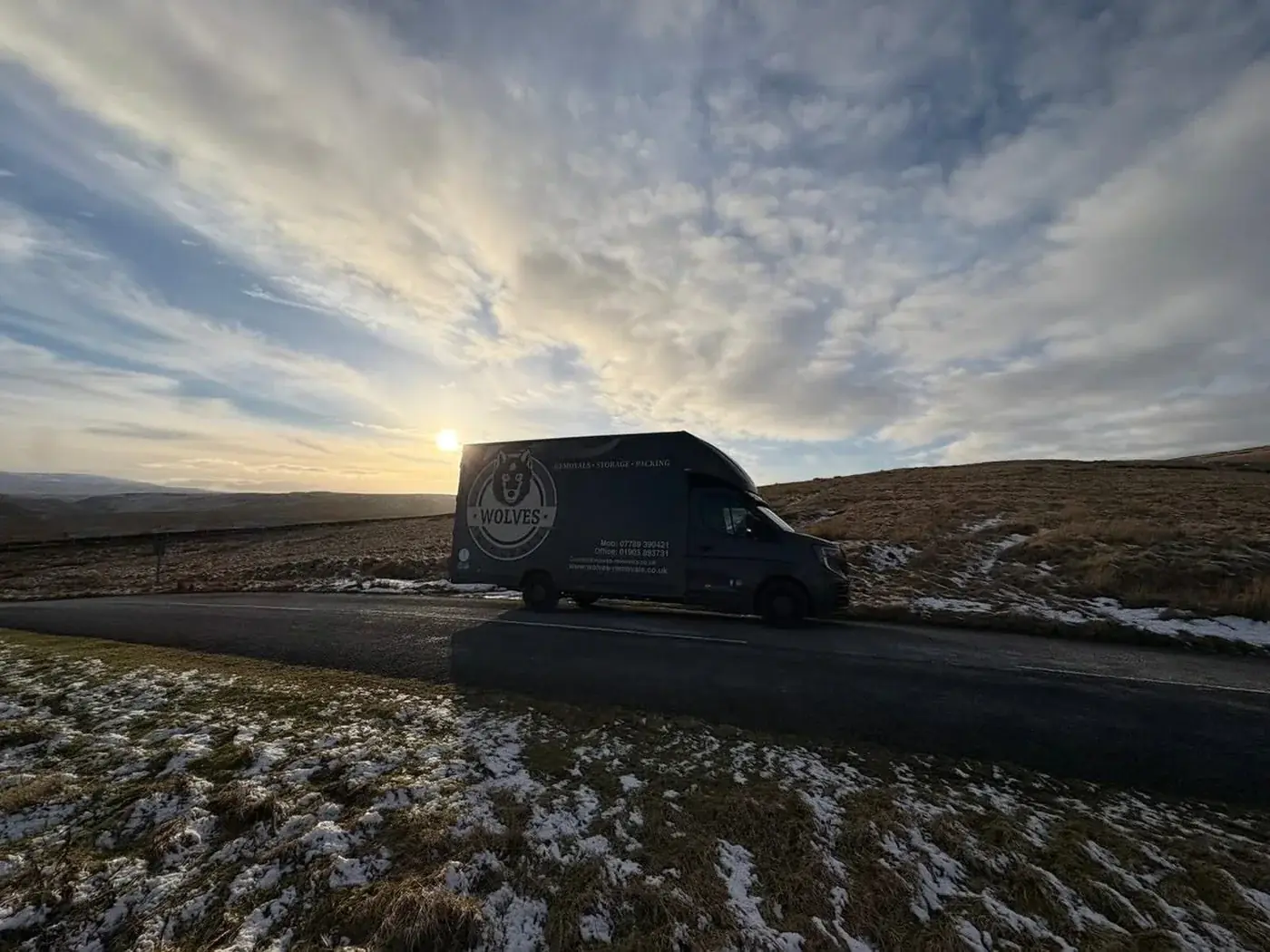 A Wolves Removals lorry silhouetted against a winter sunset on open moorland
