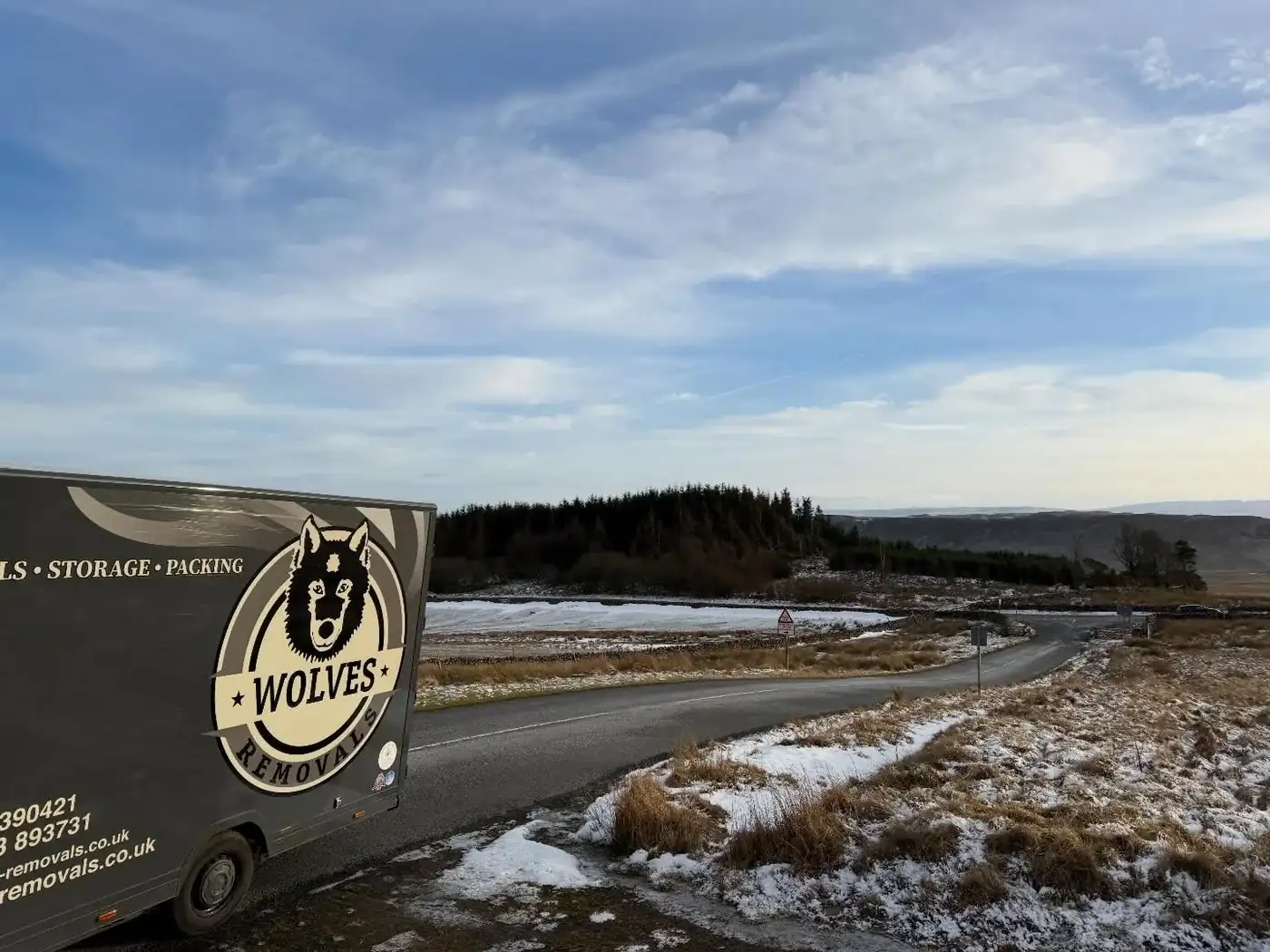 A Wolves Removals lorry beside a bend on a snow-edged Pennine road