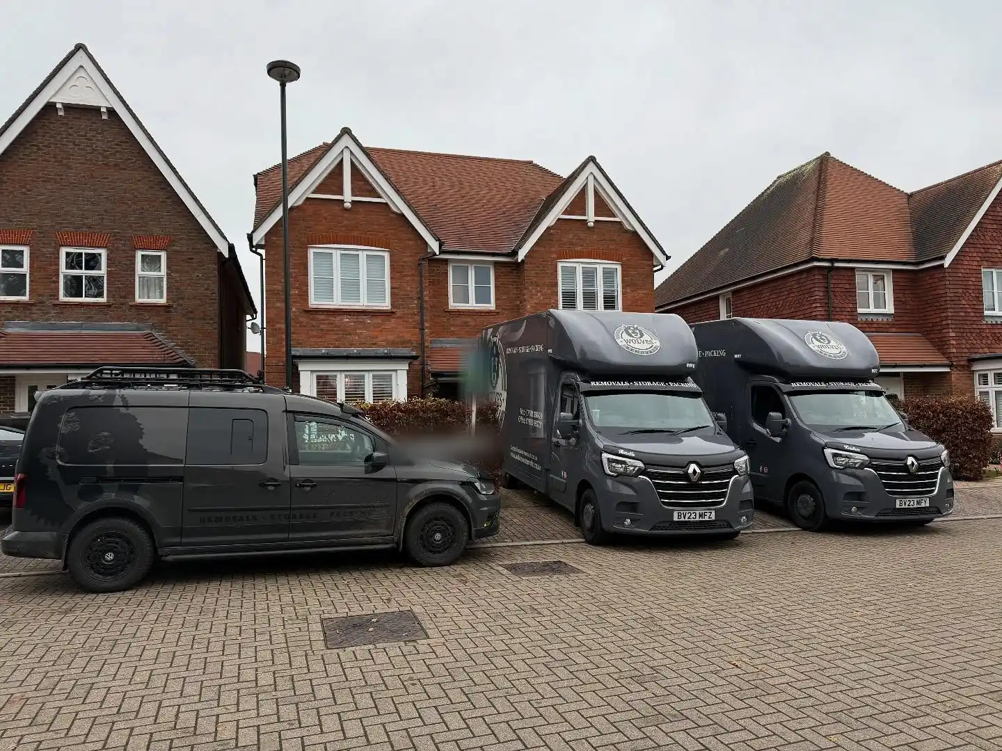 Two Wolves Removals Luton vans and a crew van parked on a block-paved street of red-brick houses during a move in Horsham