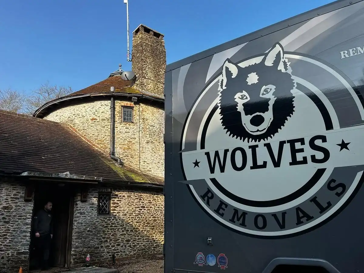 A Wolves Removals lorry parked beside a round flint house with a conical roof and stone chimney on a bright winter day