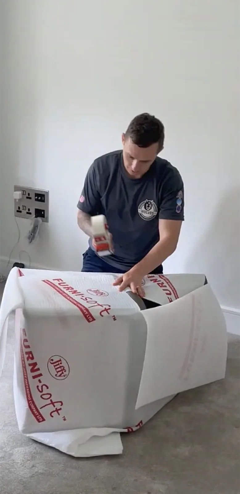A Wolves Removals packer taping Furni-Soft padding around a furniture item for export