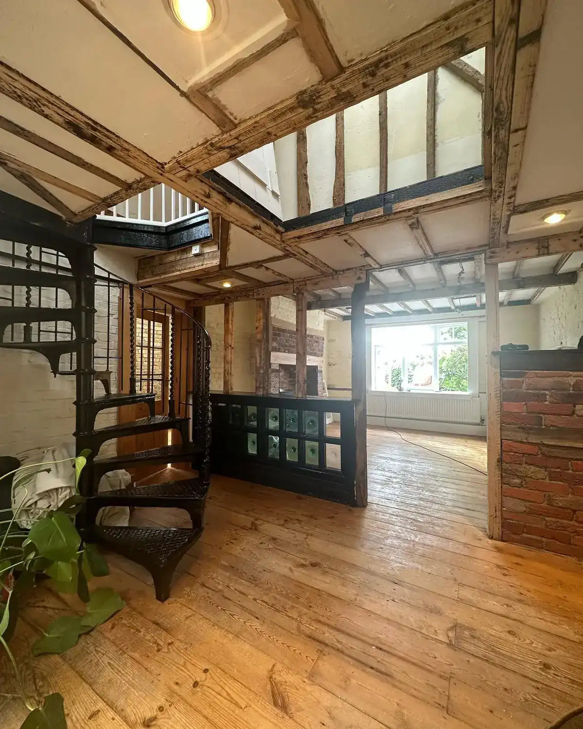 The interior of a timber-framed Chichester house with exposed beams, whitewashed brick and a black cast-iron spiral staircase