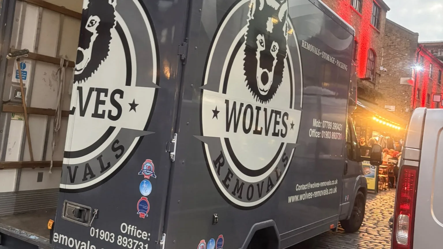 The open back of a Wolves Removals lorry beside lit market stalls at Camden Market