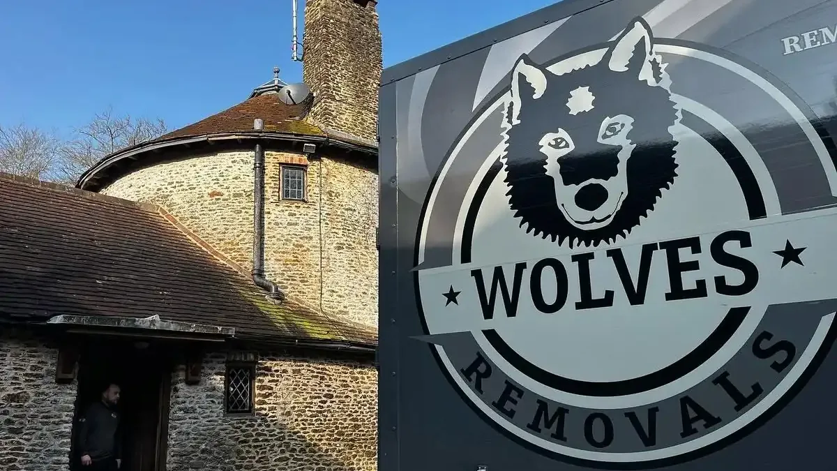 A Wolves Removals lorry with the wolf-head logo parked beside an old stone roundhouse on a sunny day