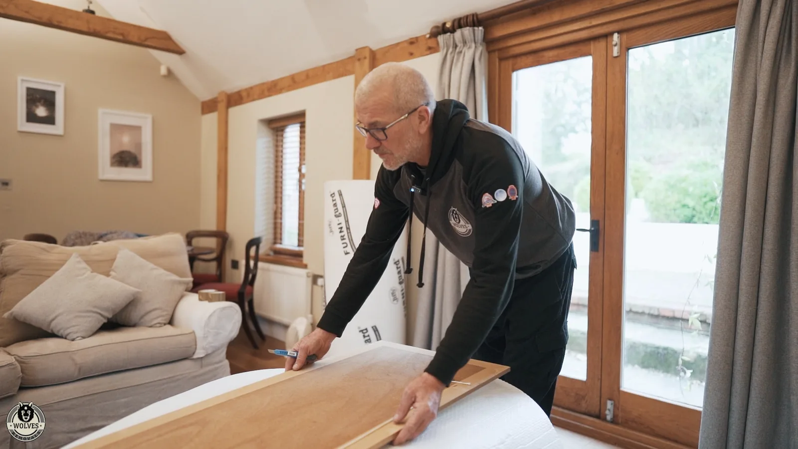 Mover wrapping a sofa in protective covering in a bright lounge with garden doors